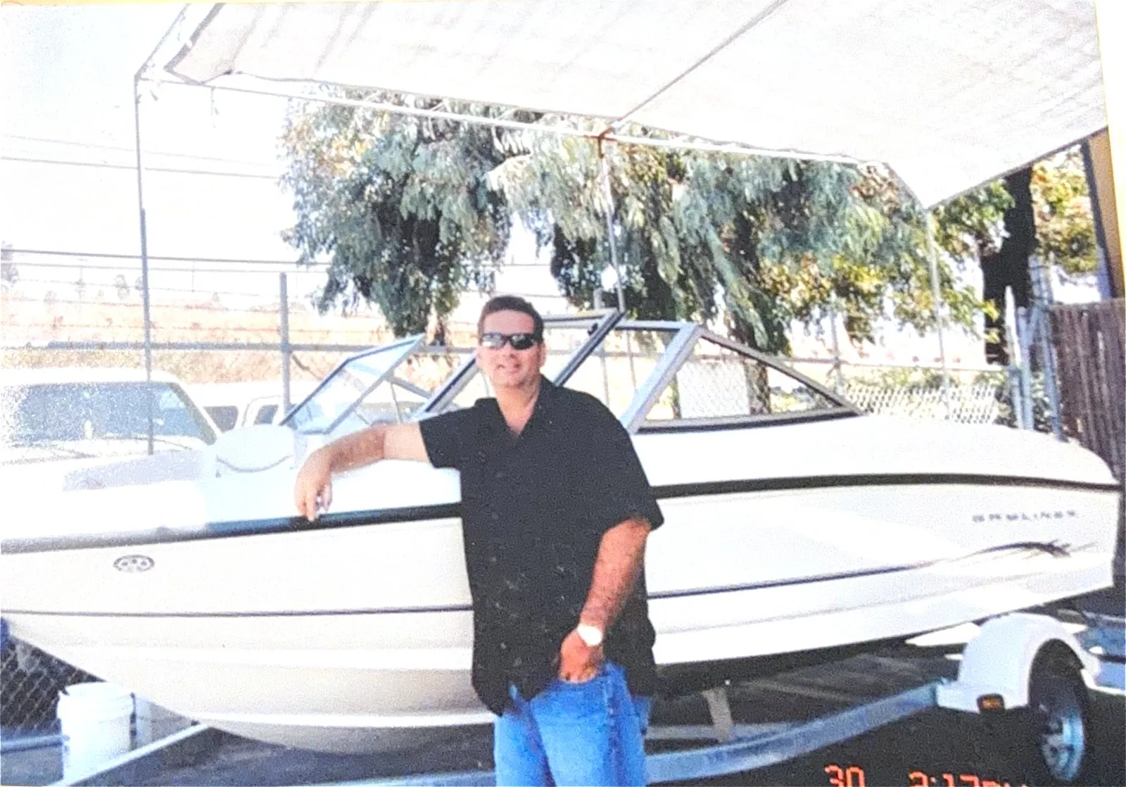 Augusto Otaduy Sr. leaning on the bow of a Bayliner bowrider on its trailer in the storage yard
