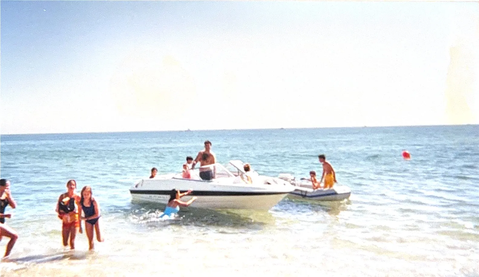Children wading around a bowrider anchored just off the beach on a bright day