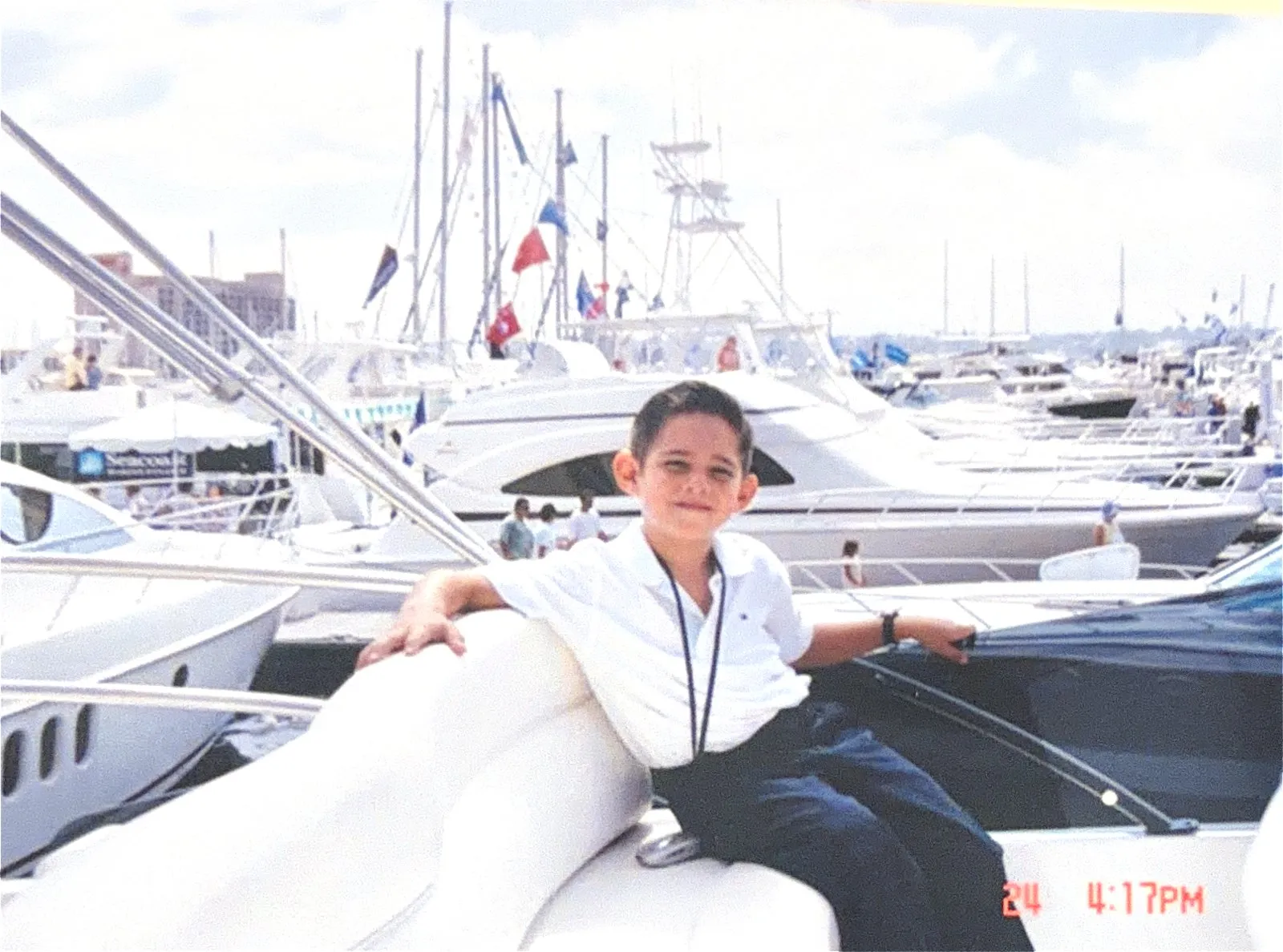 A young Gus Otaduy seated on the bow of a yacht at a crowded boat show marina