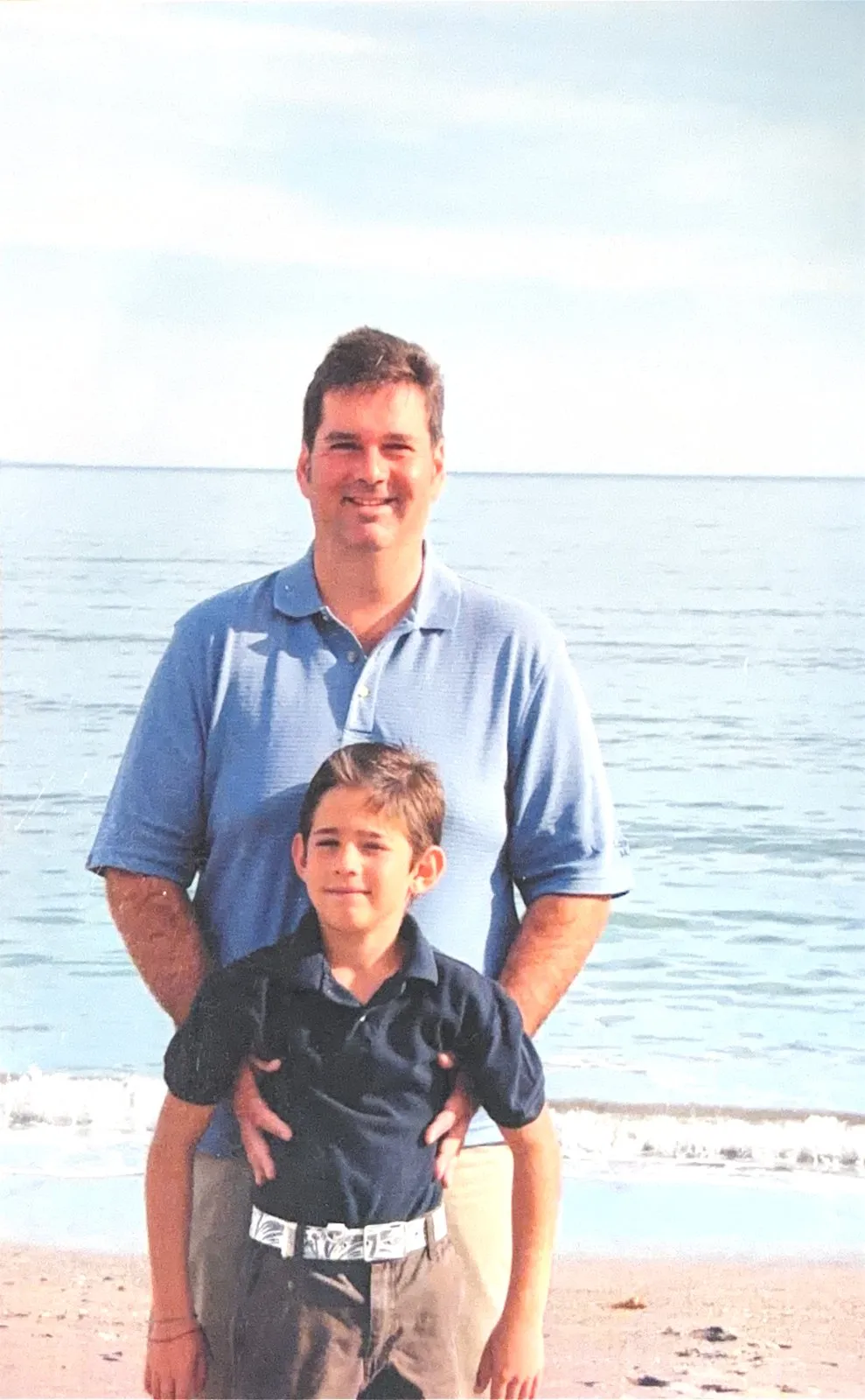 Augusto Otaduy Sr. standing with a young Gus at the water's edge on the beach