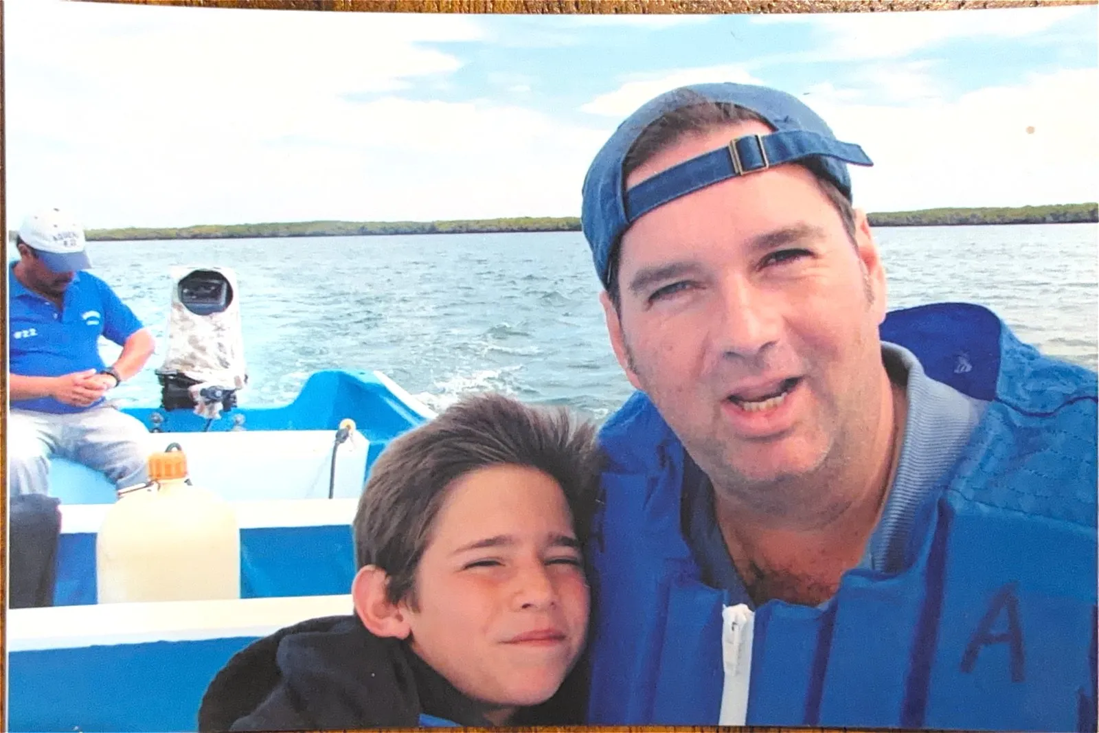 Augusto Otaduy Sr. and a young Gus leaning into the frame aboard a blue panga, mangroves and water behind them