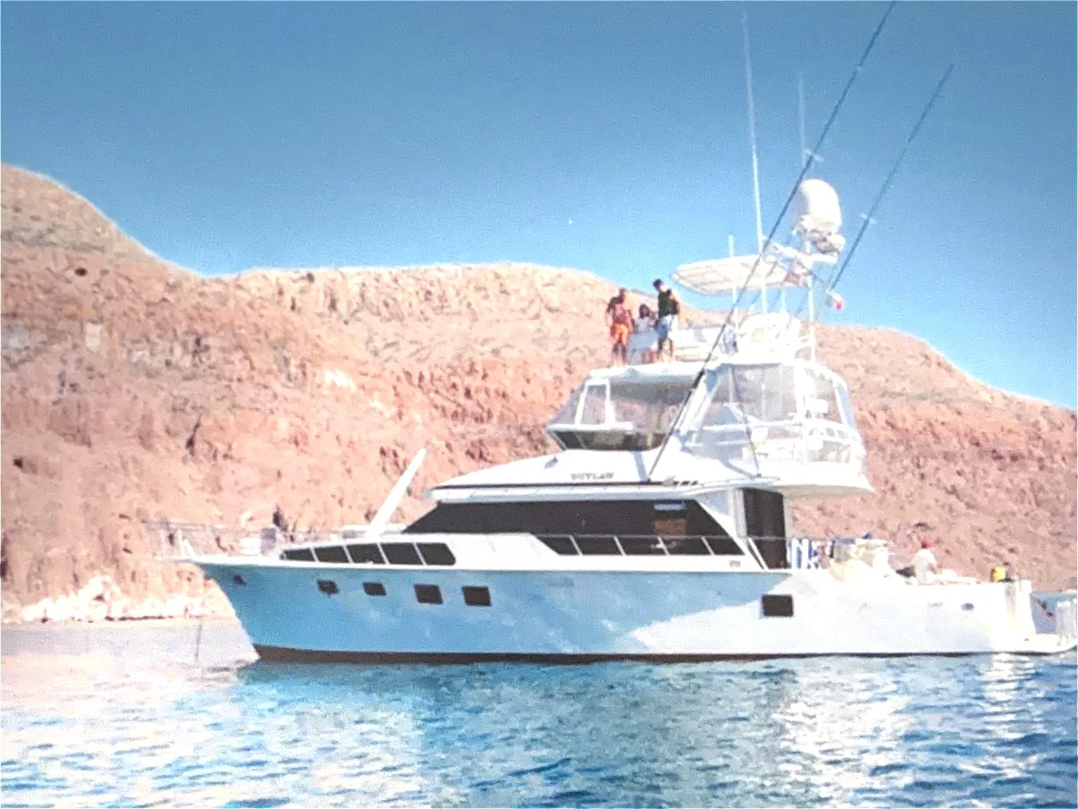 A sportfisher with tuna tower close to shore beneath red rock cliffs