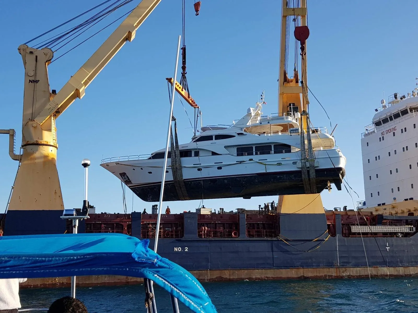 A Benetti motor yacht suspended from a crane as she is loaded aboard a transport ship
