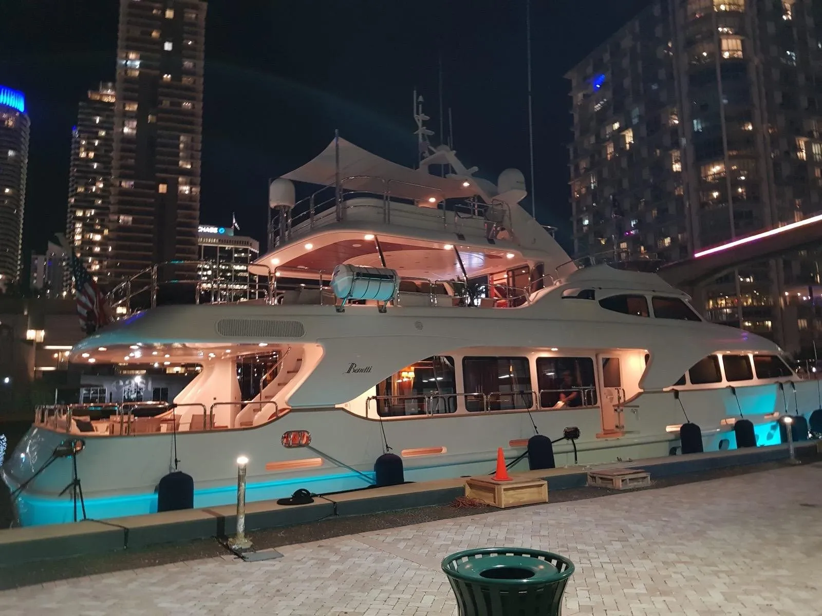A Benetti motor yacht lit up alongside at night with the Miami skyline behind her