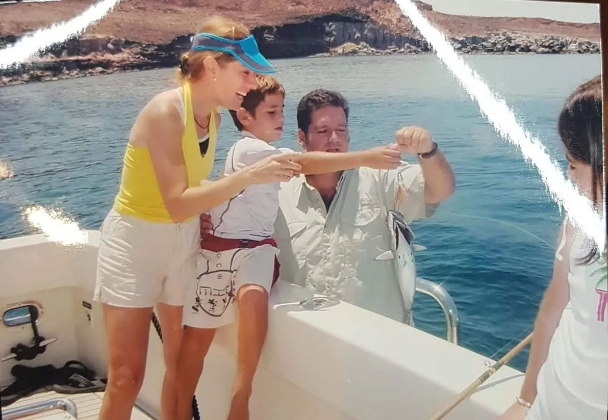 The Otaduy family aboard a boat together, holding a fish just caught, with island cliffs behind