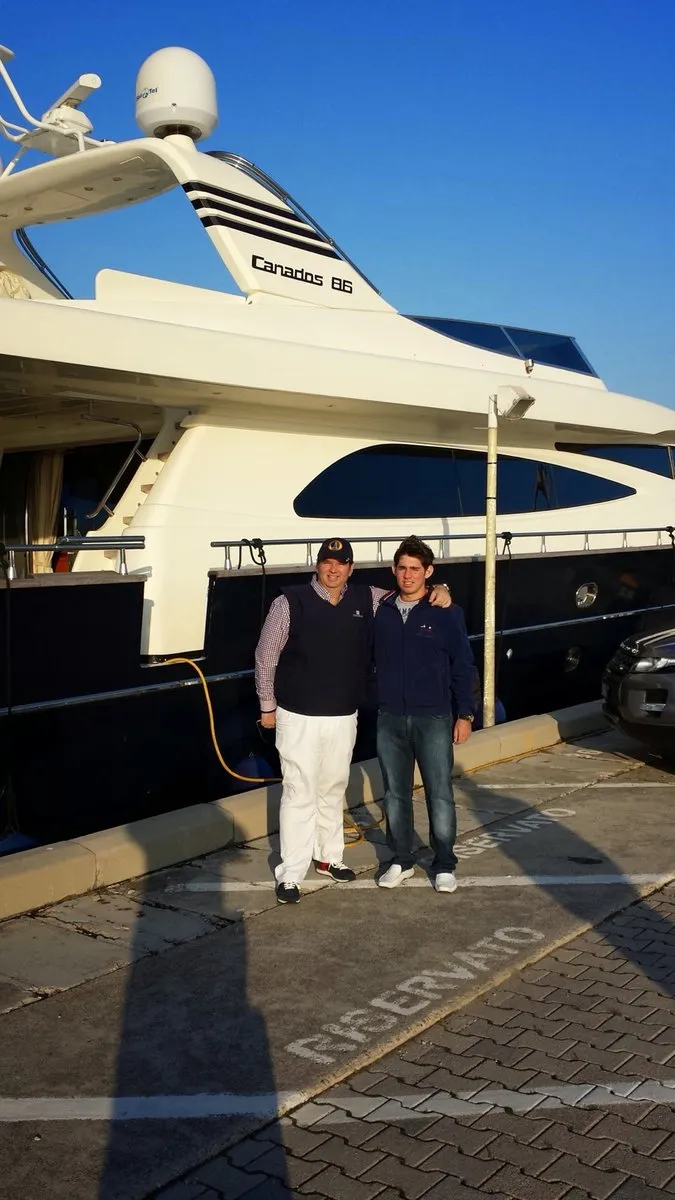 Father and son standing together beneath the flybridge of Catari, a Canados 86, on delivery day