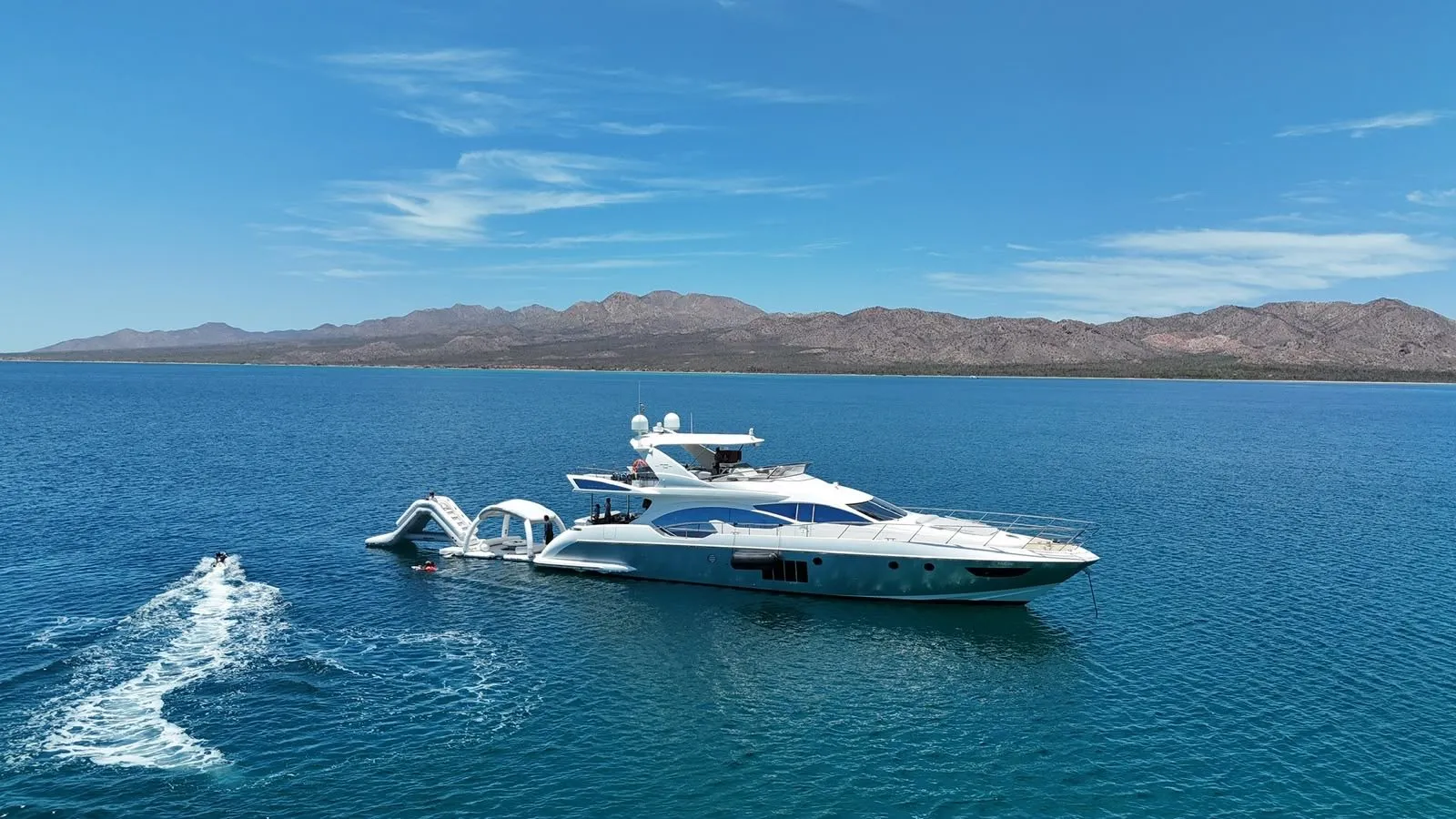 Cardinale at anchor in a bay with desert mountains behind, aerial view