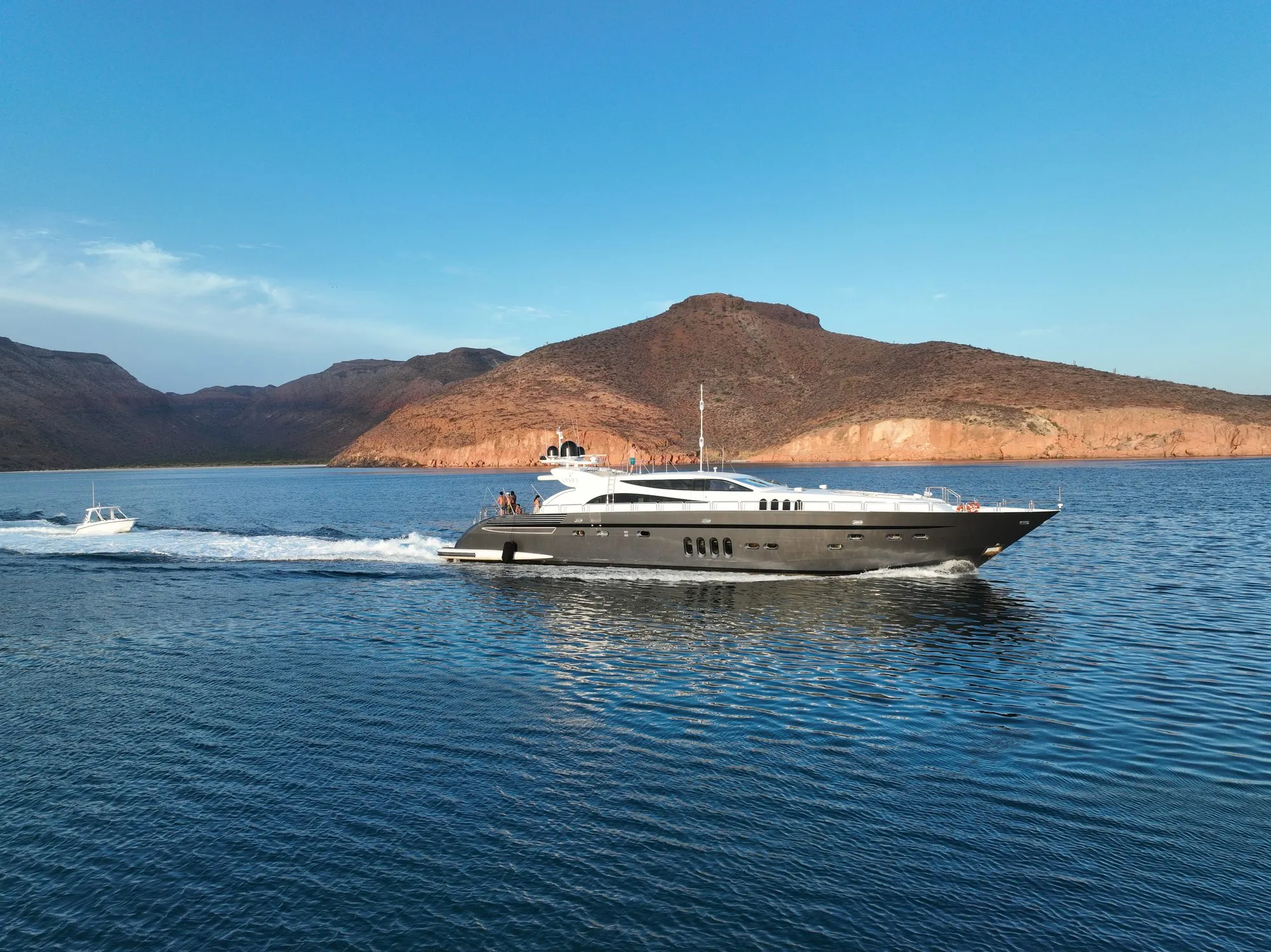 GO at anchor beneath red desert mountains with a tender passing