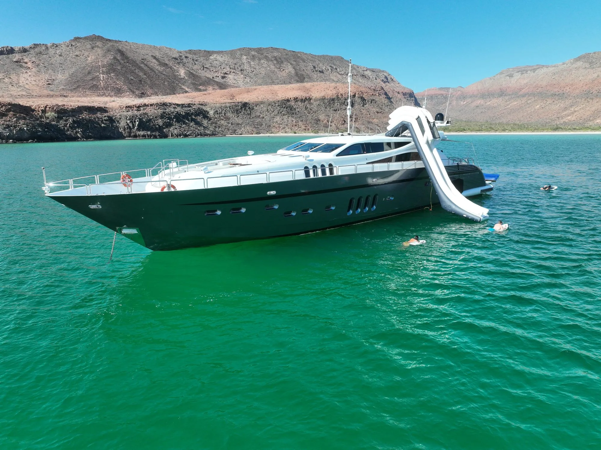 Bow view of GO at anchor with swimmers and waterslide in emerald water