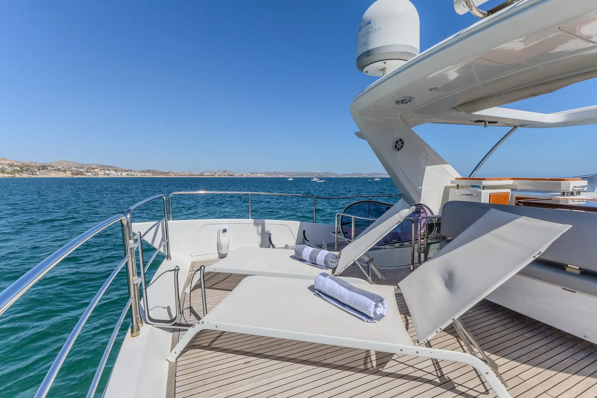 Foredeck sun loungers on Cardinale with rolled towels and coastline beyond