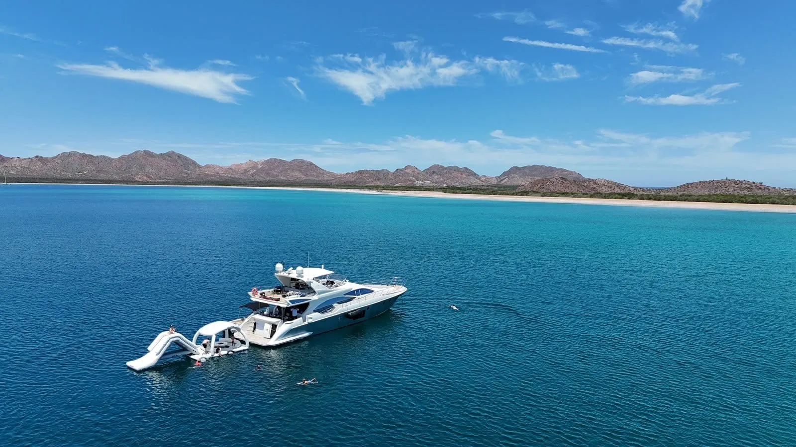 Guests swimming beside Cardinale at anchor near a beach, aerial view