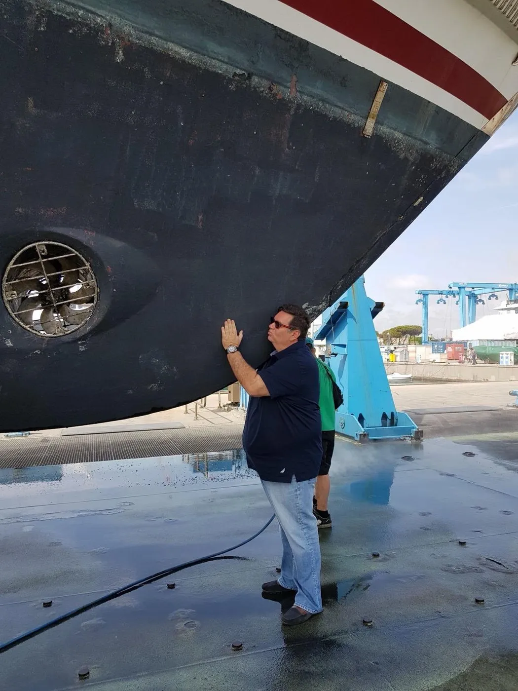 A hand resting on the hull of a yacht hauled out on stands in a boatyard
