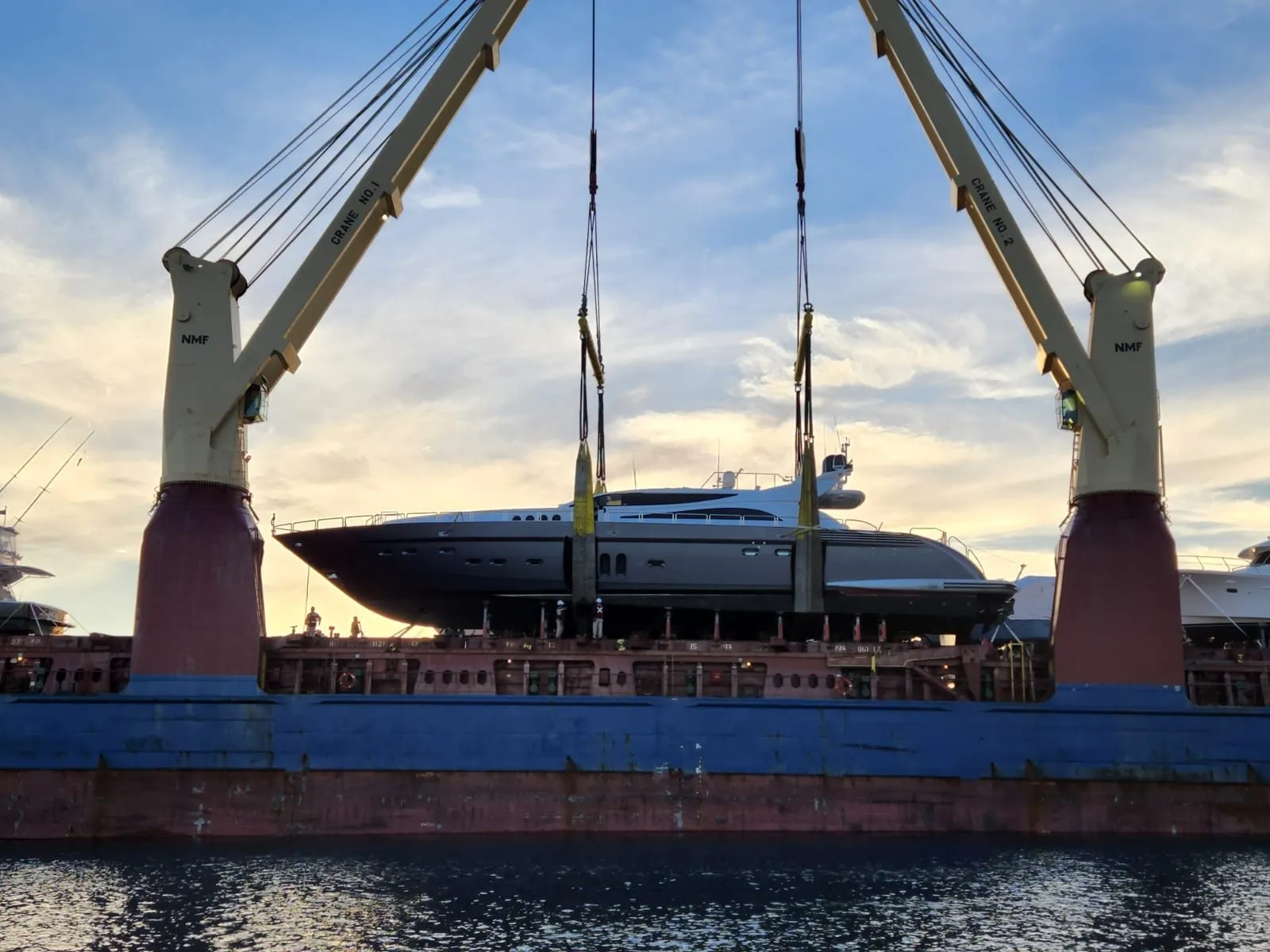 Motor yacht lifted between cargo ship cranes at sunset