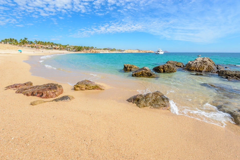 Large rocks on the beach and leading into the bright blue waters of Chileno Bay.