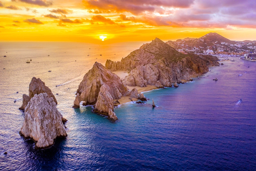 Lovers beach Cabo at sunset with bright orange in the sky and purple waters.