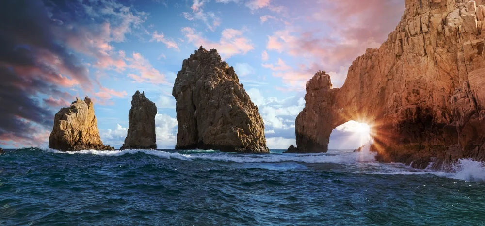 The arch of Cabo San Lucas and surrounding rocks as the sun sets in the background.