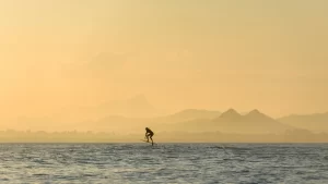 A person fliteboarding on the ocean with an orange sky.