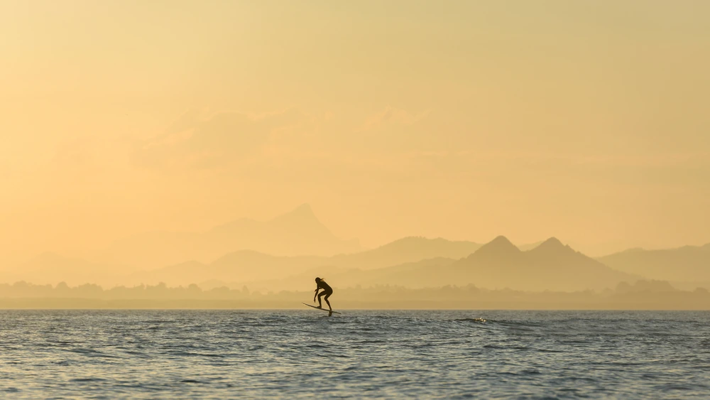 A person fliteboarding on the ocean with an orange sky.