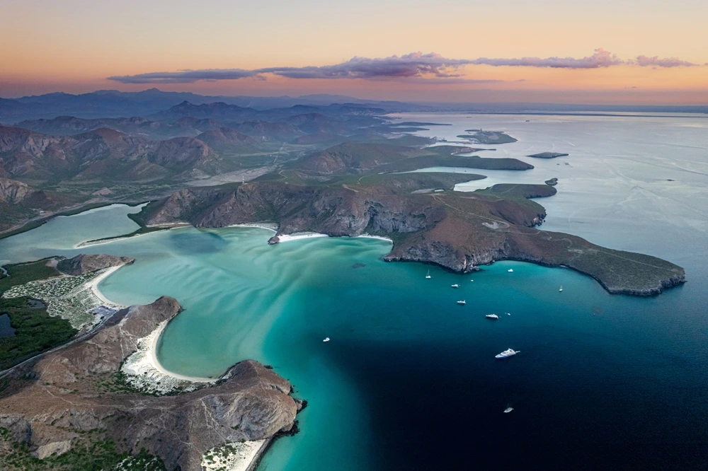 A birds-eye view of Balandra Beach with turquoise water and orange sky.
