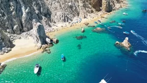 Vessels on clear blue water near a crowded beach in Cabo.